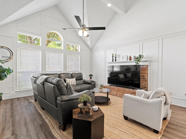 living room featuring ceiling fan, hardwood / wood-style floors, beam ceiling, high vaulted ceiling, and a brick fireplace