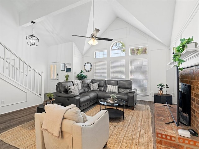 living room with a fireplace, ceiling fan with notable chandelier, wood-type flooring, and high vaulted ceiling