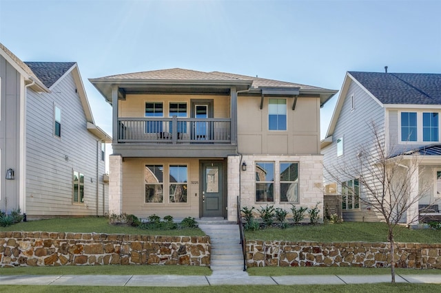 view of front facade with roof with shingles, a balcony, a front lawn, and stucco siding