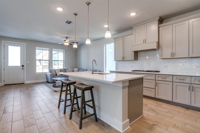 kitchen featuring hanging light fixtures, an island with sink, sink, and a breakfast bar