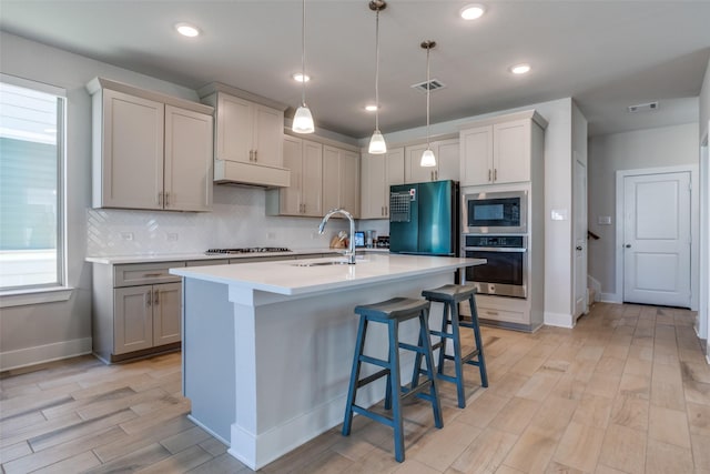 kitchen with sink, a breakfast bar area, gray cabinetry, hanging light fixtures, and stainless steel appliances