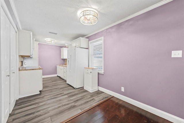 kitchen featuring hardwood / wood-style floors, white cabinetry, ornamental molding, white fridge with ice dispenser, and a textured ceiling