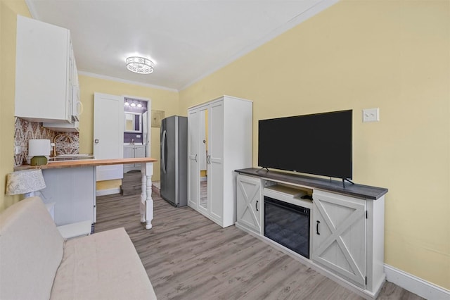 kitchen with stainless steel refrigerator, crown molding, light hardwood / wood-style flooring, and white cabinets