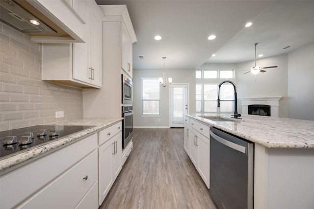 kitchen with sink, a kitchen island with sink, stainless steel appliances, custom range hood, and white cabinets