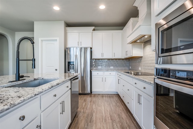 kitchen with white cabinetry, sink, custom range hood, and appliances with stainless steel finishes