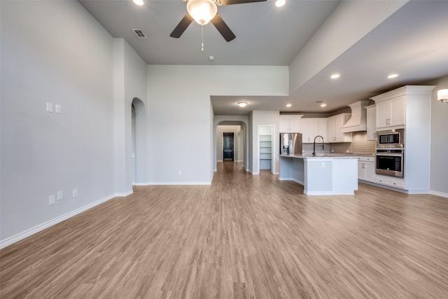 kitchen featuring tasteful backsplash, white cabinetry, custom exhaust hood, a kitchen island with sink, and stainless steel appliances