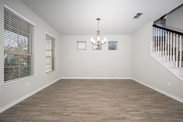 spare room with an inviting chandelier and dark hardwood / wood-style floors