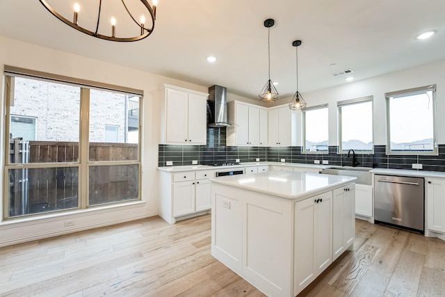 kitchen with dishwasher, sink, white cabinets, a center island, and wall chimney range hood