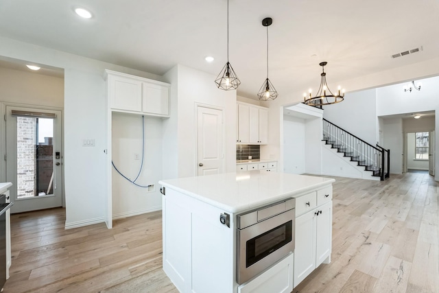 kitchen with a center island, hanging light fixtures, light wood-type flooring, stainless steel microwave, and white cabinets