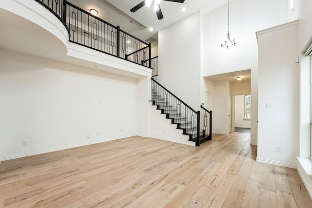 interior space with a towering ceiling, ceiling fan with notable chandelier, and light hardwood / wood-style flooring