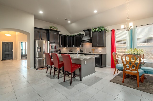 kitchen with an inviting chandelier, custom exhaust hood, arched walkways, vaulted ceiling, and appliances with stainless steel finishes