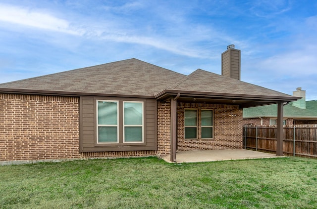 rear view of property featuring a patio, fence, a yard, a chimney, and brick siding