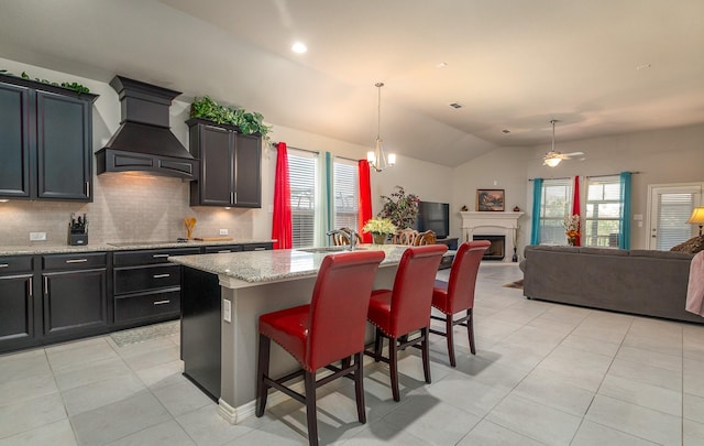 kitchen with backsplash, open floor plan, vaulted ceiling, custom exhaust hood, and a kitchen island with sink