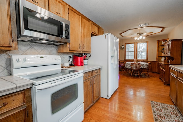 kitchen with white appliances, ceiling fan, backsplash, tile countertops, and light wood-type flooring