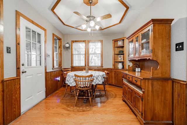 dining space with ceiling fan, light hardwood / wood-style flooring, and wood walls