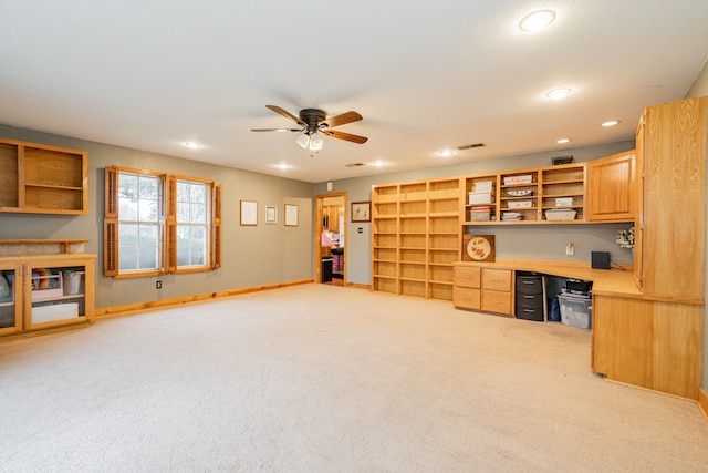 home office with built in desk, light colored carpet, and ceiling fan