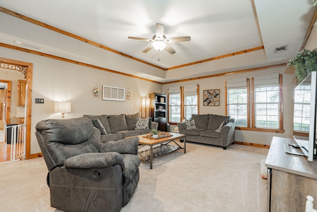 living room with ceiling fan, ornamental molding, a tray ceiling, and light carpet