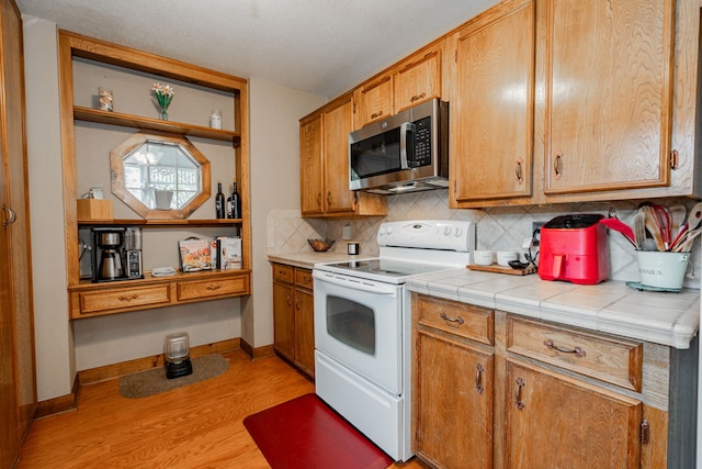 kitchen featuring tasteful backsplash, white range with electric cooktop, tile countertops, and light wood-type flooring