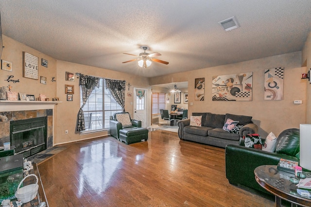 living room featuring hardwood / wood-style flooring, ceiling fan, a fireplace, and a textured ceiling