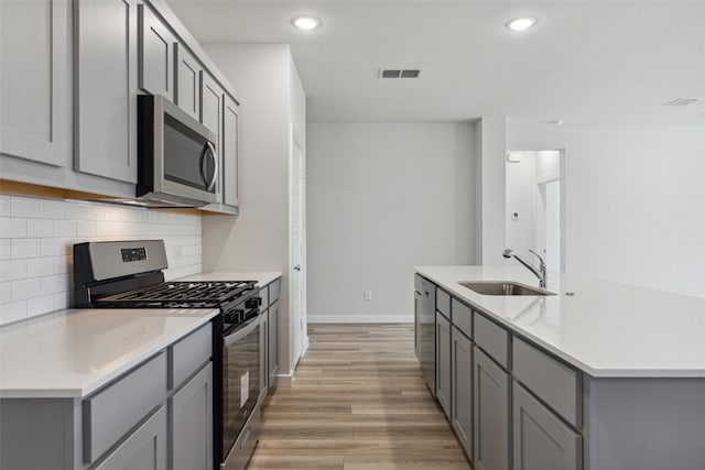 kitchen featuring appliances with stainless steel finishes, sink, gray cabinetry, and light wood-type flooring