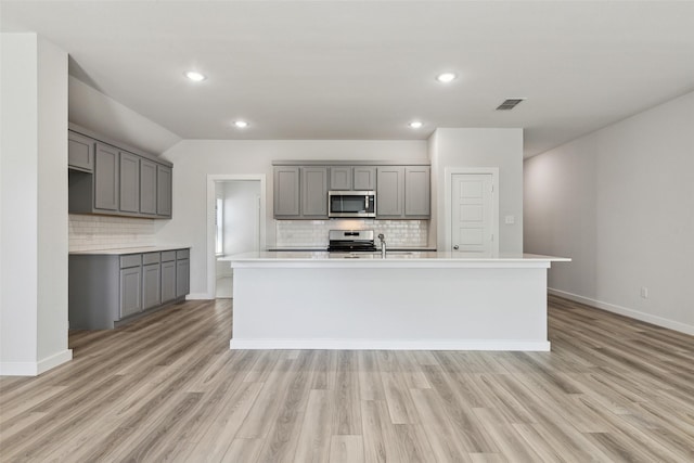 kitchen featuring backsplash, appliances with stainless steel finishes, a kitchen island with sink, and gray cabinetry