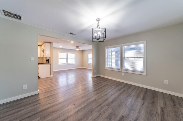 unfurnished living room featuring ceiling fan with notable chandelier and dark wood-type flooring