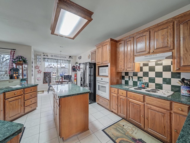 kitchen featuring white appliances, light tile patterned floors, a kitchen island, and backsplash