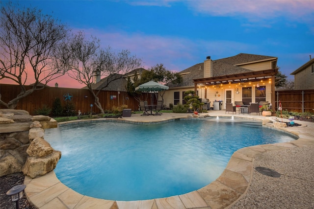 pool at dusk with pool water feature, grilling area, and a patio area