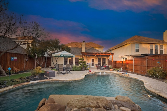 pool at dusk with a patio area and pool water feature