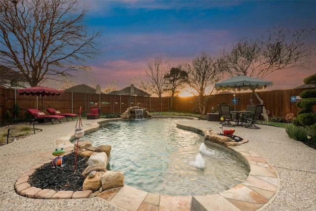 pool at dusk with pool water feature and a patio area