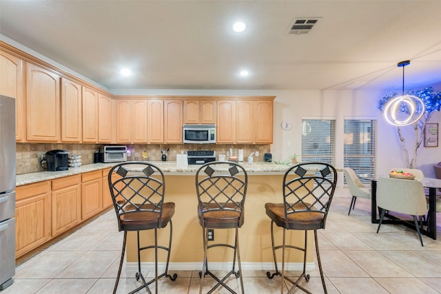 kitchen with light brown cabinetry, light tile patterned floors, appliances with stainless steel finishes, light stone countertops, and backsplash