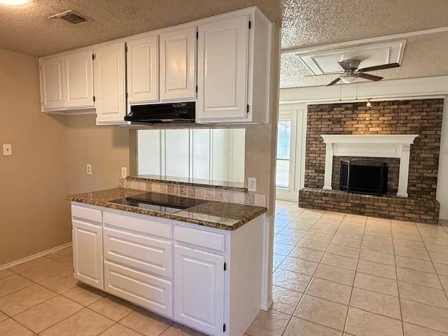 kitchen with ceiling fan, white cabinetry, a fireplace, black electric cooktop, and dark stone counters