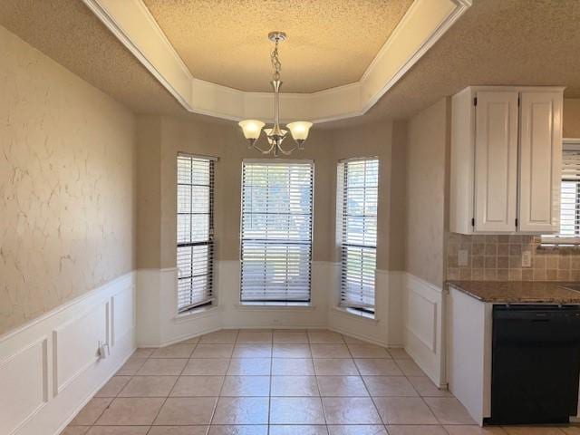 unfurnished dining area featuring a notable chandelier, a tray ceiling, a textured ceiling, and light tile patterned flooring