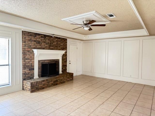 unfurnished living room featuring ceiling fan, light tile patterned floors, a brick fireplace, and a textured ceiling