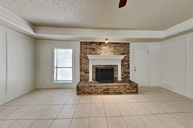 unfurnished living room featuring light tile patterned floors, ceiling fan, ornamental molding, a textured ceiling, and a brick fireplace