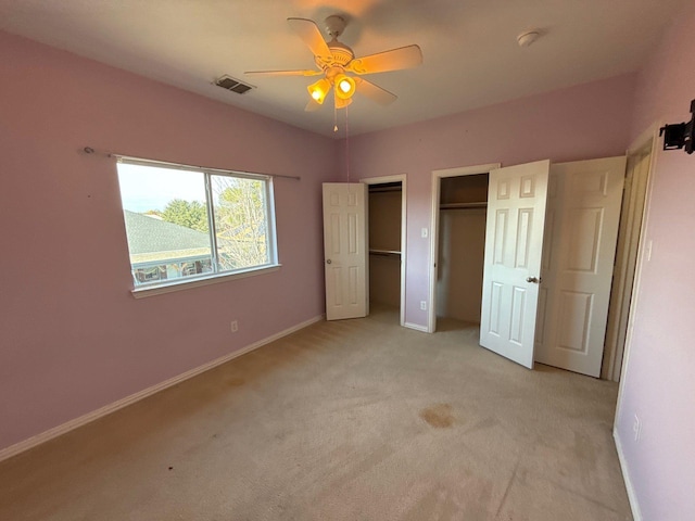 unfurnished bedroom with multiple closets, ceiling fan, and light carpet