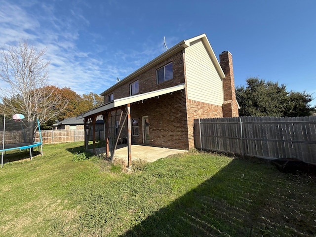 back of property with a trampoline, a yard, and a patio area