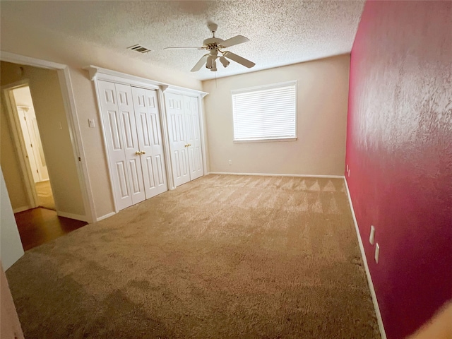 unfurnished bedroom with ceiling fan, a textured ceiling, carpet floors, and multiple closets