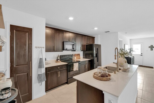 kitchen with black range with electric cooktop, dark brown cabinetry, stainless steel fridge, and an island with sink