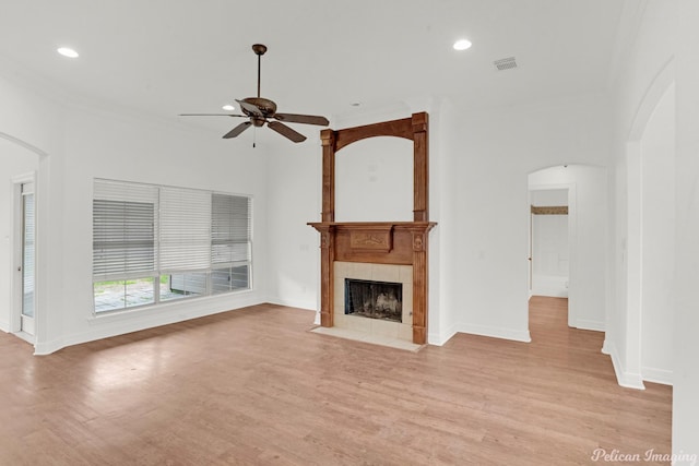 unfurnished living room with a tiled fireplace, ceiling fan, ornamental molding, and light wood-type flooring