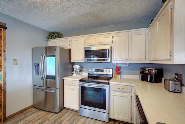 kitchen with light hardwood / wood-style floors, a textured ceiling, and appliances with stainless steel finishes