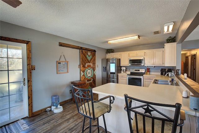 kitchen with appliances with stainless steel finishes, sink, a breakfast bar area, dark hardwood / wood-style flooring, and kitchen peninsula