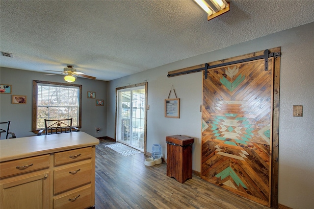 kitchen with ceiling fan, a barn door, a textured ceiling, and dark hardwood / wood-style flooring