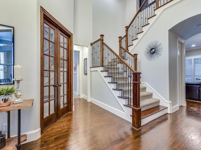 foyer entrance with a towering ceiling, wood-type flooring, and french doors