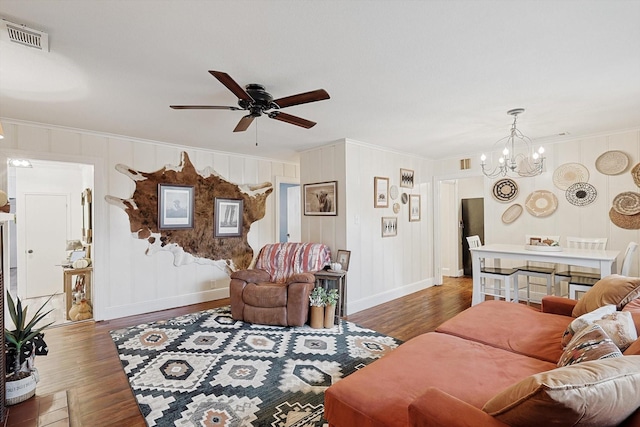 living room with dark wood-type flooring, crown molding, and ceiling fan with notable chandelier