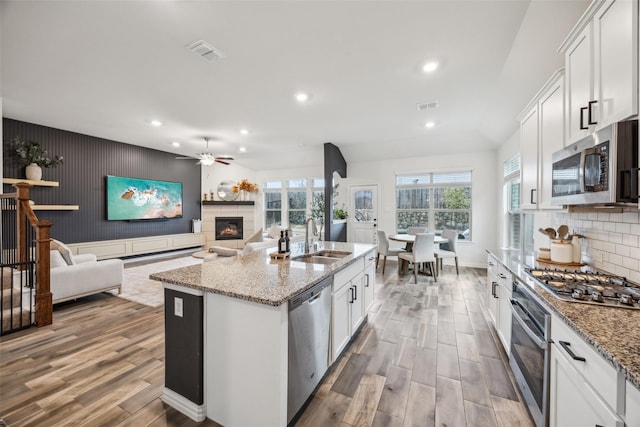 kitchen featuring sink, appliances with stainless steel finishes, a kitchen island with sink, light stone counters, and white cabinets