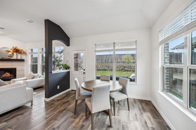 dining area with a tile fireplace, vaulted ceiling, and dark hardwood / wood-style flooring