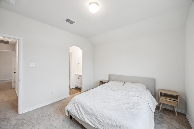 bedroom featuring ensuite bath, vaulted ceiling, and light carpet