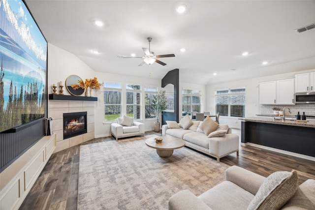 living room featuring a tile fireplace, dark wood-type flooring, sink, and ceiling fan