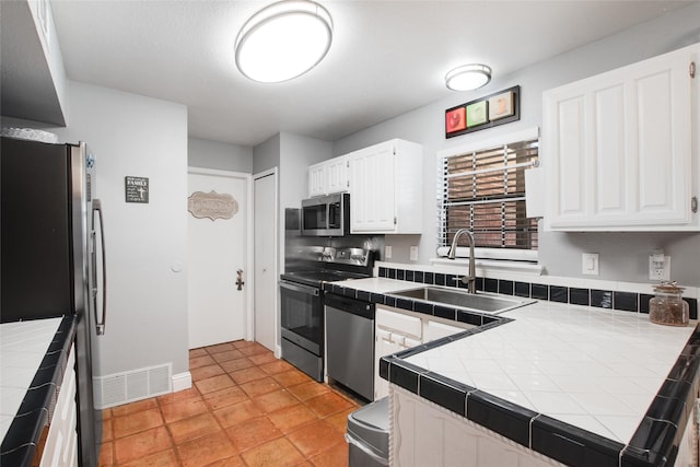 kitchen featuring appliances with stainless steel finishes, tile counters, sink, and white cabinets